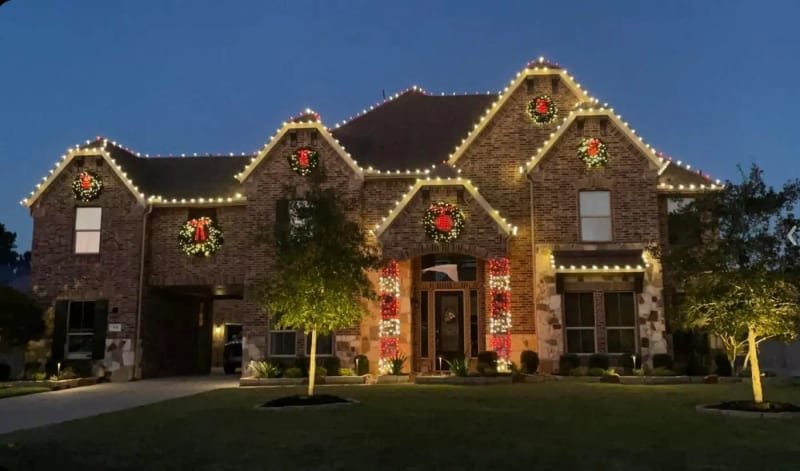 Brick house with wreaths over each gable and the roofline outlined in lights