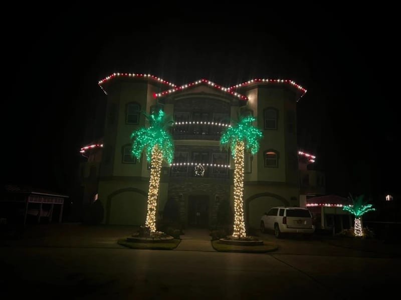Castle-style white house with the roofline outlined and palm trees wrapped in lights
