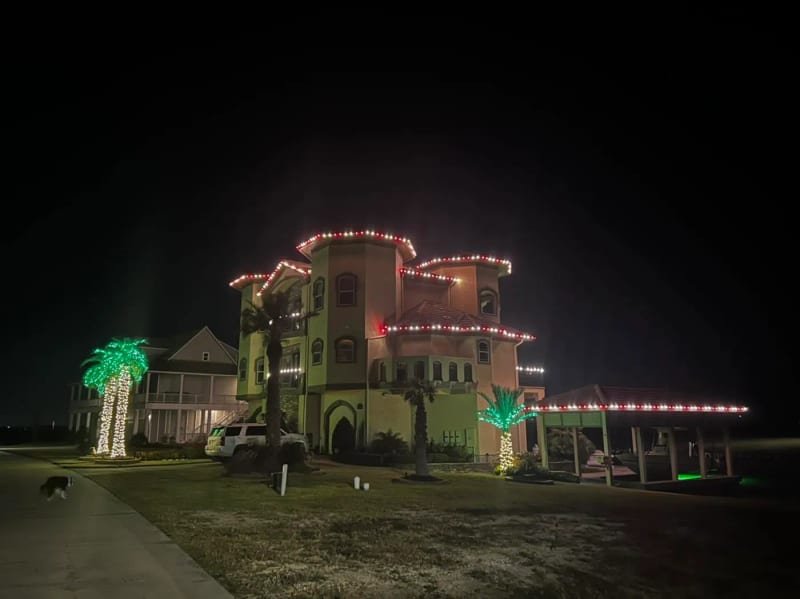 Castle-like house with lights along the roof and wrapped palm trees out front