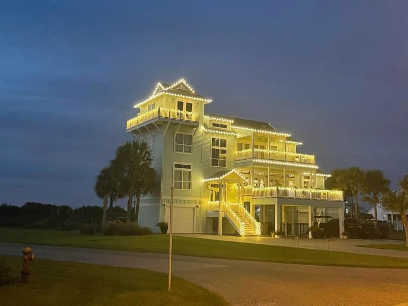 Four-story house with its roof and deck railings wrapped in Christmas lights