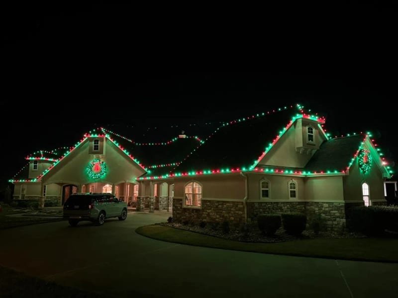 Ranch-style house with its roofline lit and a large wreath on the gable