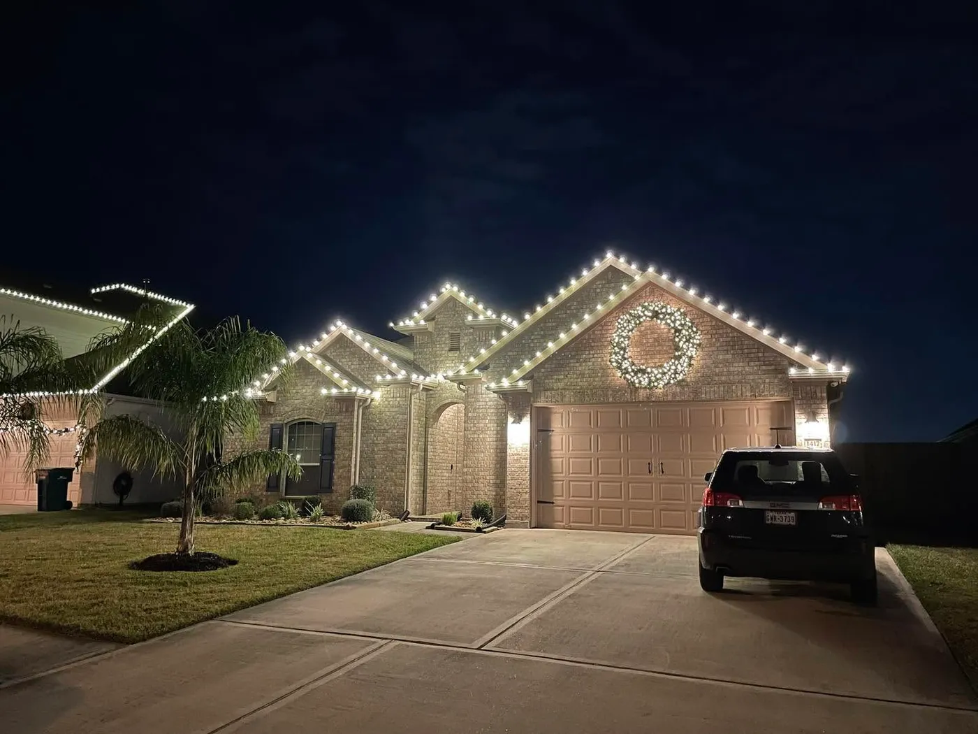 Small house Christmas lights outlining the roof with a large wreath over the garage