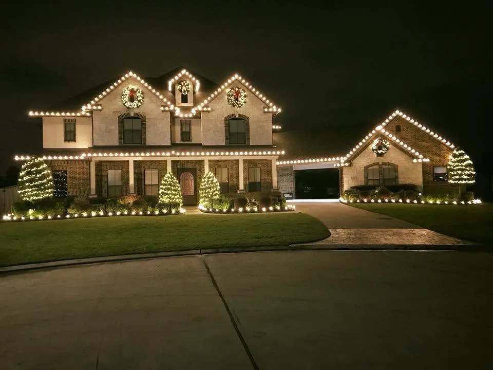 Two-story house with detached garage wrapped in Christmas lights, landscaping also