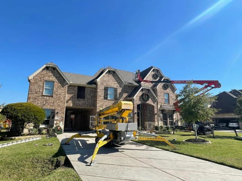 Crew installing lights and gable wreaths on a two-story house