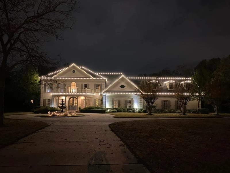 Two-story ranch house with its roof outlined in lights and a lit bird bath