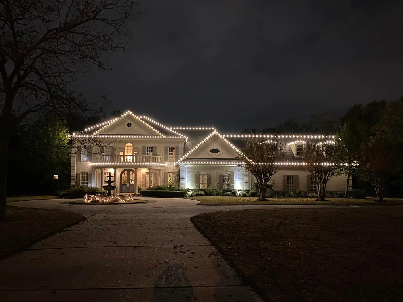 Two-story nice ranch house with roof outlined in Christmas lights and bird bath